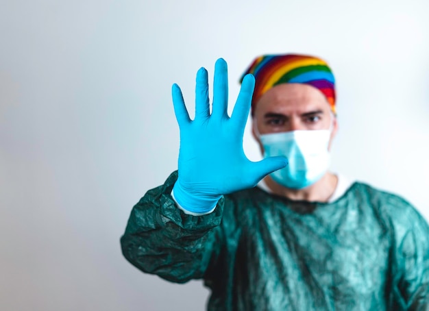 Chirurg Arzt mit Schutzmaske und Regenbogenbandana auf dem Kopf, der seine Hand in blauem Handschuh zeigt Arzt stoppt HIV-Virus oder Coronavirus mit Prävention Lgbtq-Menschenrechtskonzept