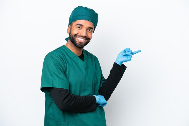 Chirurg Brasilianischer Mann in grüner Uniform isoliert auf weißem Hintergrund, der mit dem Finger zur Seite zeigt