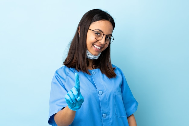 Chirurg Frau über blaue Wand, die einen Finger zeigt und hebt