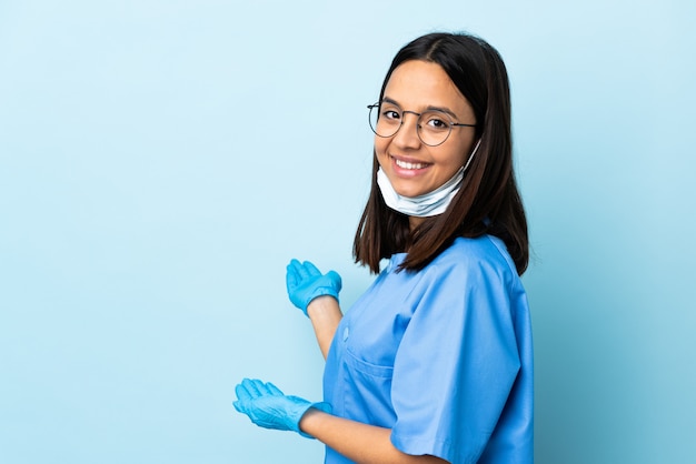 Chirurg Frau über isolierte blaue Wand, die Hände zur Seite ausstreckt, um einzuladen, zu kommen