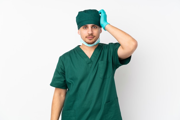 Chirurg in grüner Uniform an weißer Wand mit Ausdruck von Frustration und Unverständnis