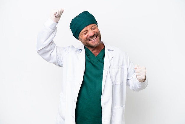Chirurg mittleren Alters in grüner Uniform isoliert auf weißem Hintergrund, der einen Sieg feiert