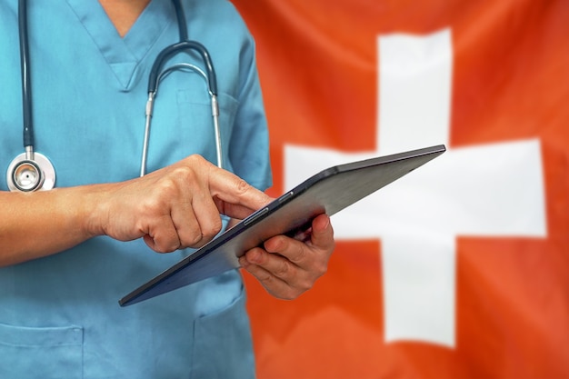 Chirurg oder Arzt mit einem digitalen Tablet auf dem Hintergrund der Schweiz Flagge