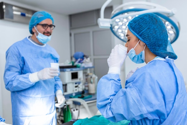 Chirurgenteam mit chirurgischer Maske am Trinkwasser des Operationssaals nach erfolgreicher Operation. Junge Ärztin in chirurgischer Uniform im Operationssaal des Krankenhauses.