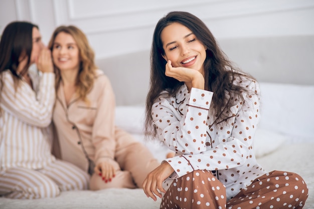 Chismes. Dos niñas sentadas en una cama y hablando de su amiga a sus espaldas