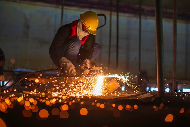 Chispa de corte de metal de trabajador masculino en la placa de acero del fondo del tanque con destello de luz de corte cerca del desgaste