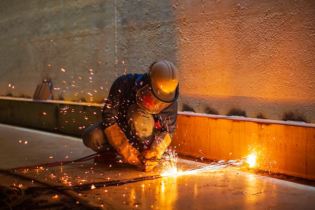 Chispa de corte de metal de trabajador masculino en la placa de acero del fondo del tanque con destello de luz de corte de cerca, use guantes protectores y máscara en un espacio confinado lateral