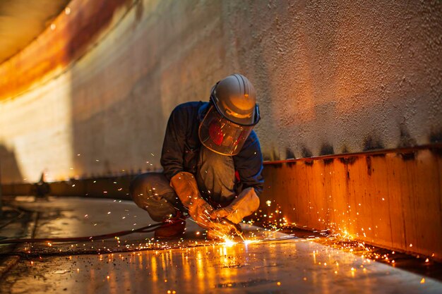 Chispa de corte de metal de trabajador masculino en la placa de acero del fondo del tanque con destello de luz de corte de cerca, use guantes protectores y máscara