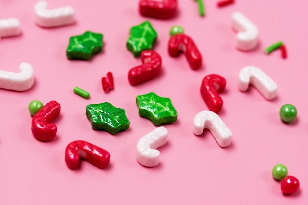 Chispitas de colores sobre fondo rosa Decoración de confitería en forma de bastón de caramelo y acebo