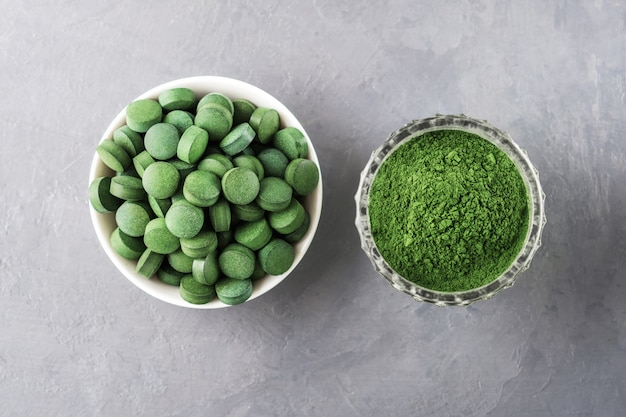 Chlorella oder Spirulina in Form von Tabletten und Pulver auf grauem Betonhintergrund.