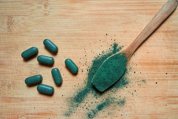 Chlorella- oder Spirulina-Tabletten und -Pulver in einem Holzlöffel auf hellem Holzhintergrund ergänzen