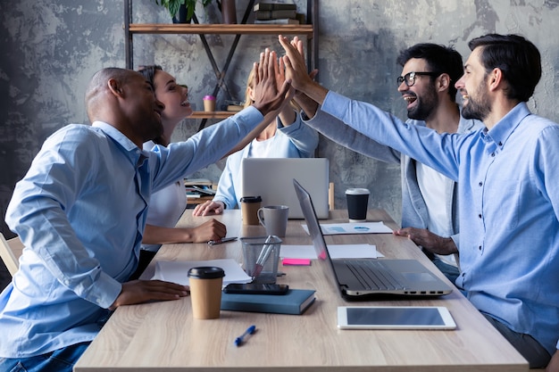 Choca esos cinco para el éxito Grupo diverso de colegas de negocios que se dan cinco en un símbolo de unidad y sonríen mientras trabajan en la sala de juntas.