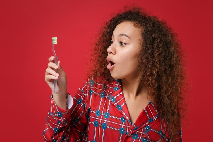 Foto chocada jovem afro-americana em homewear de pijama posando enquanto descansava em casa isolado no fundo da parede vermelha no estúdio. relaxe o conceito de estilo de vida de bom humor. mock up espaço de cópia. segure a escova de dentes.