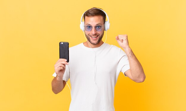 Chocada, rindo e comemorando o sucesso, ouvindo música com fones de ouvido e um smartphone