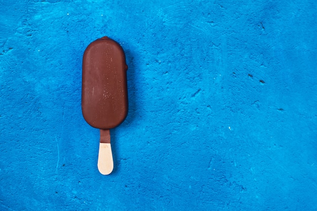 Foto chocolate amargo mergulhado em picolé em um fundo azul clássico texturizado com espaço de cópia