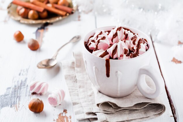 Chocolate caliente con caramelos de malvavisco en taza de cerámica rústica blanca sobre superficie de madera clara vieja. Enfoque selectivo.