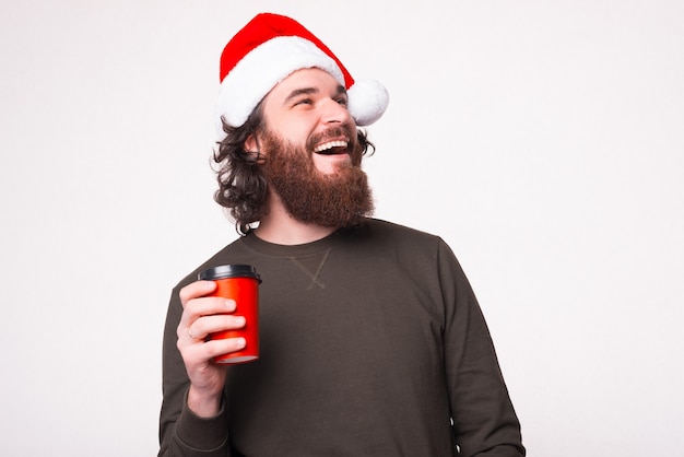 Chocolate caliente en un clima frío. Feliz el hombre barbudo con sombrero de navidad está sosteniendo una taza para llevar.