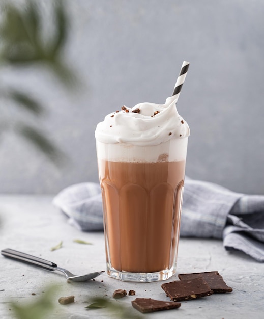 Chocolate caliente con crema batida y trozos de chocolate en un vaso alto sobre un fondo azul con una rama Vista frontal y espacio para copiar