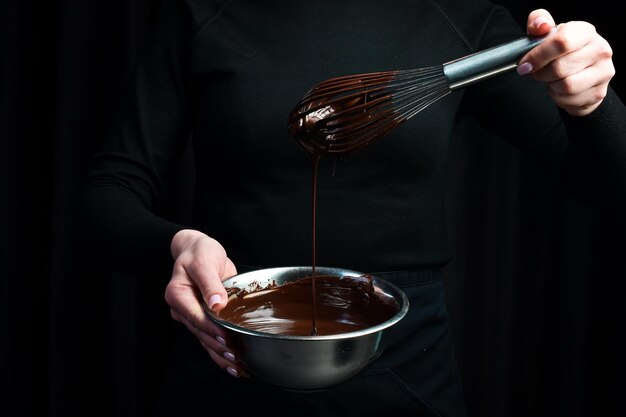 Chocolate caliente derretido en un tazón y un batidor de cocina utensilios de cocina sobre un fondo negro