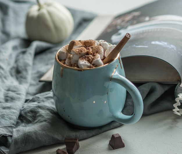 Chocolate caliente con malvavisco en una taza azul con una rama de canela.