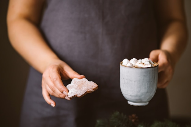 Chocolate caliente con malvaviscos y galletas de jengibre en manos femeninas