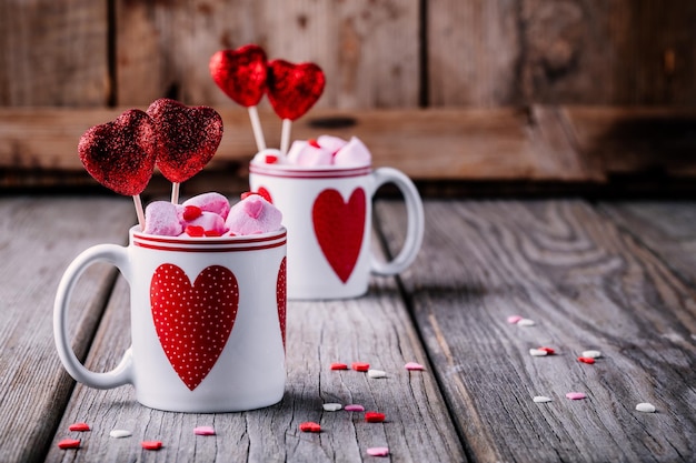 Chocolate caliente con malvaviscos rosas en tazas con corazones sobre un fondo de madera para el día de San Valentín