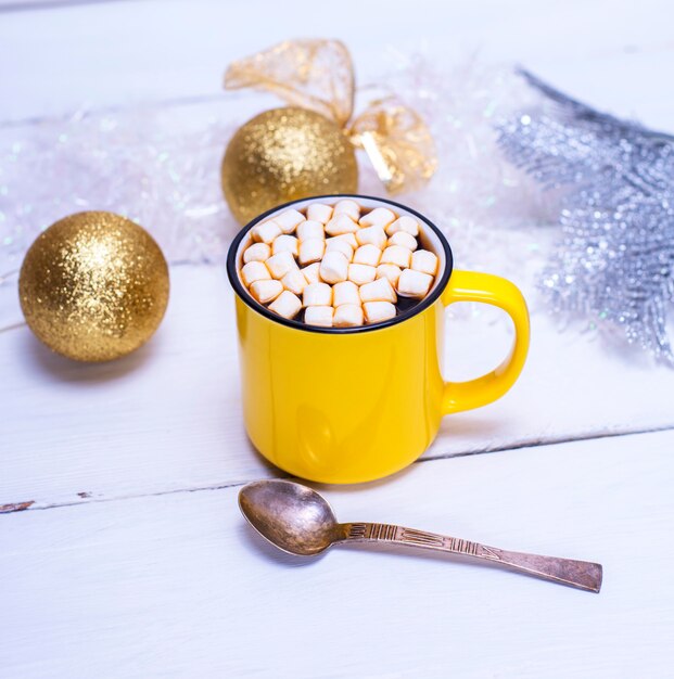 Chocolate caliente con malvaviscos en una taza amarilla y juguetes navideños