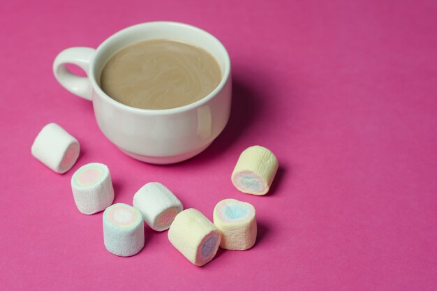 Chocolate caliente con malvaviscos en una taza de cerámica sobre fondo de papel rosa