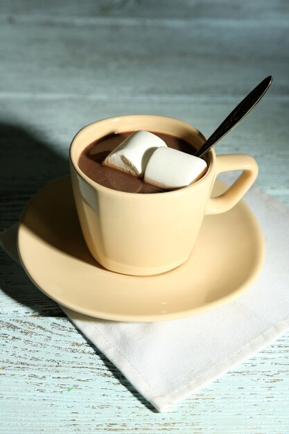 Chocolate caliente con malvaviscos en taza, sobre fondo de madera