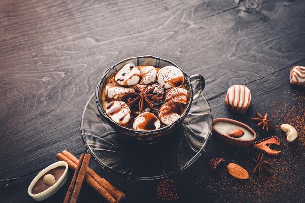 Chocolate caliente con marshmallou, nueces, especias, konfeti de chocolate, canela. En el escritorio de madera negro.