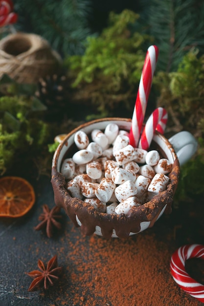 Chocolate caliente de Navidad en una taza negra con naranjas caramelizadas, ramas de abeto y bastón de caramelo sobre fondo oscuro, enfoque selectivo