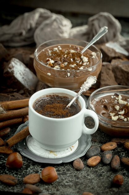 Chocolate caliente sobre un fondo antiguo en una composición con cacao en grano y nueces.