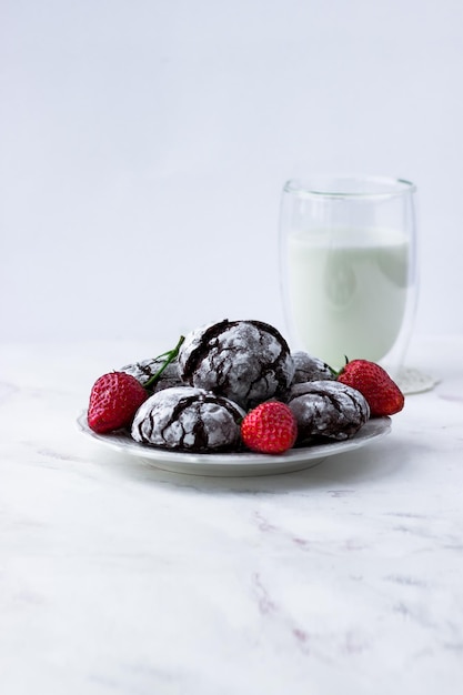 Chocolate Cracks Cookies auf einem weißen Marmortisch Köstliche Kekse eine Tasse Milch und Erdbeeren