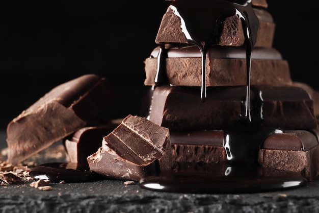 Chocolate derretido derramando em um pedaço de barras de chocolate em uma mesa escura