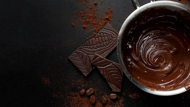 Chocolate derretido en una olla con trozos de chocolate alrededor sobre una superficie oscura