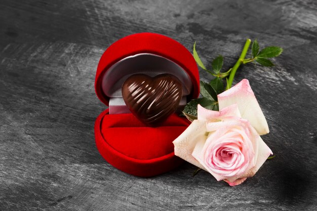 Chocolate en forma de corazón en una caja roja para un anillo, una rosa rosa sobre un fondo oscuro. Concepto amor por el chocolate