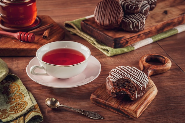 Un chocolate de galleta de miel brasileña mordido cubierto sobre la mesa de madera con una taza de té de porcelana, miel de abeja y canela - Pao de mel