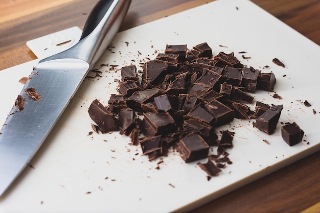 Foto chocolate que foi cortado em cubos grosseiros em uma tábua de cortar branca