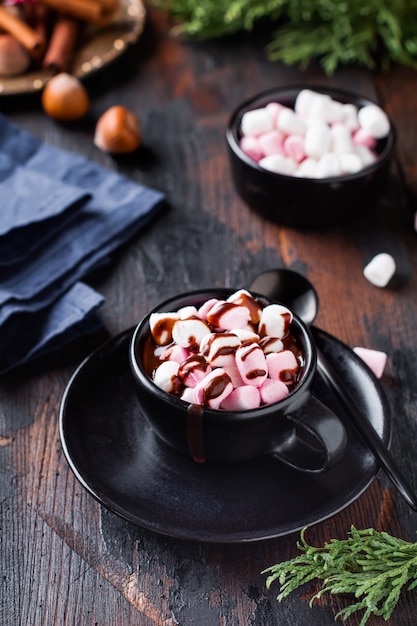 Chocolate quente com balas de marshmallow em copo de cerâmica preta na velha superfície de madeira escura. foco seletivo.