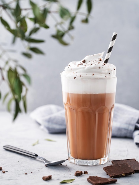 Chocolate quente com chantilly e pedaços de chocolate em um copo alto sobre um fundo azul com um ramo Vista frontal