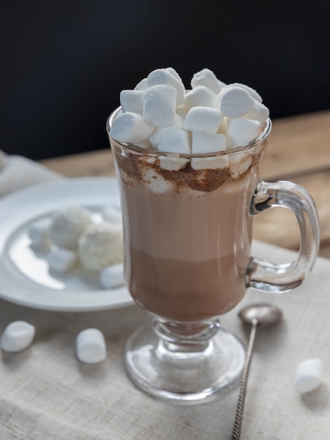Chocolate quente com marshmallow em copo de vidro sobre mesa de madeira Bebida quente e galho de abeto