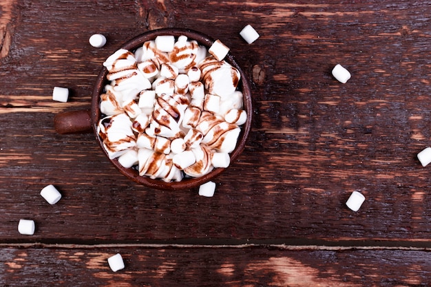 Chocolate quente com marshmallow no copo marrom no fundo de madeira