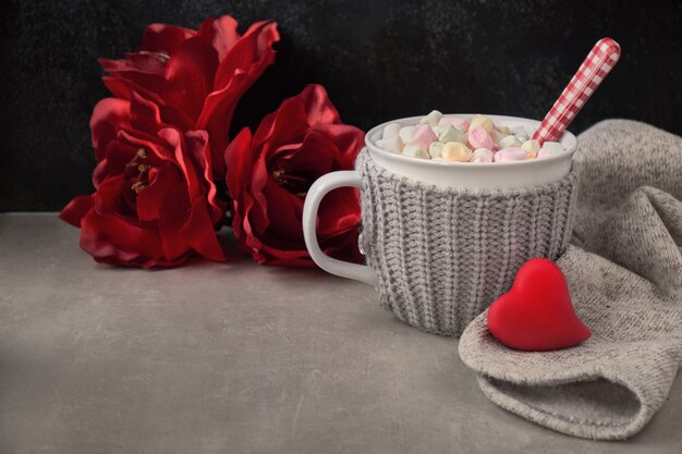 Chocolate quente com marshmallows, coração vermelho no copo em cima da mesa