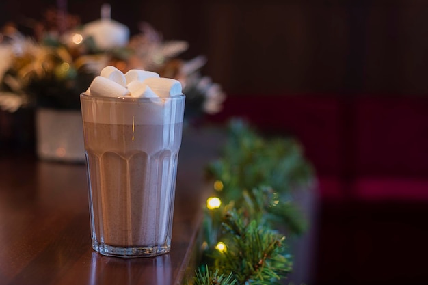 Chocolate quente com marshmallows em um vidro transparente em um café no fundo da decoração de ano novo.