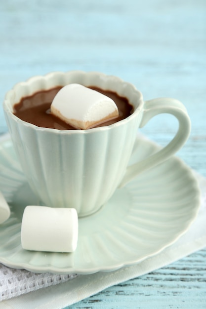 Chocolate quente com marshmallows na caneca, mesa de madeira de cor, superfície clara