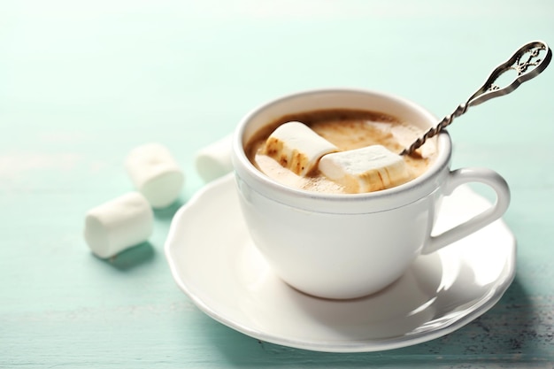 Chocolate quente com marshmallows na caneca, na cor de fundo de madeira