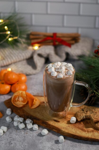 chocolate quente em uma caneca de vidro com mini marshmallows na placa de madeira, fundo de natal turva