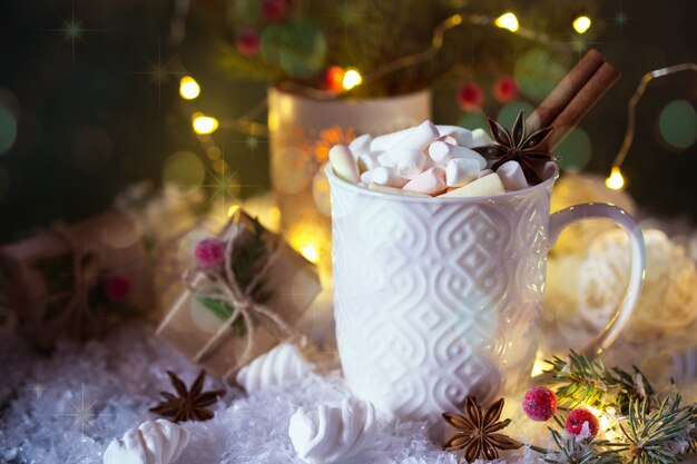 Chocolate quente em uma xícara branca com marshmallows e presentes de Natal na luz brilhante. Bebida de Natal.