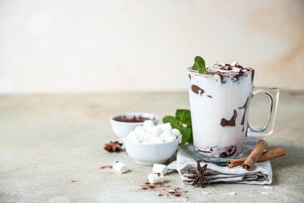 Chocolate quente ou cacau em copo de vidro com marshmallow, canela e hortelã