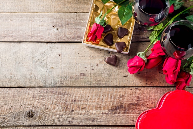 Chocolate, rosas, copos de vinho e caixa de coração na mesa de madeira